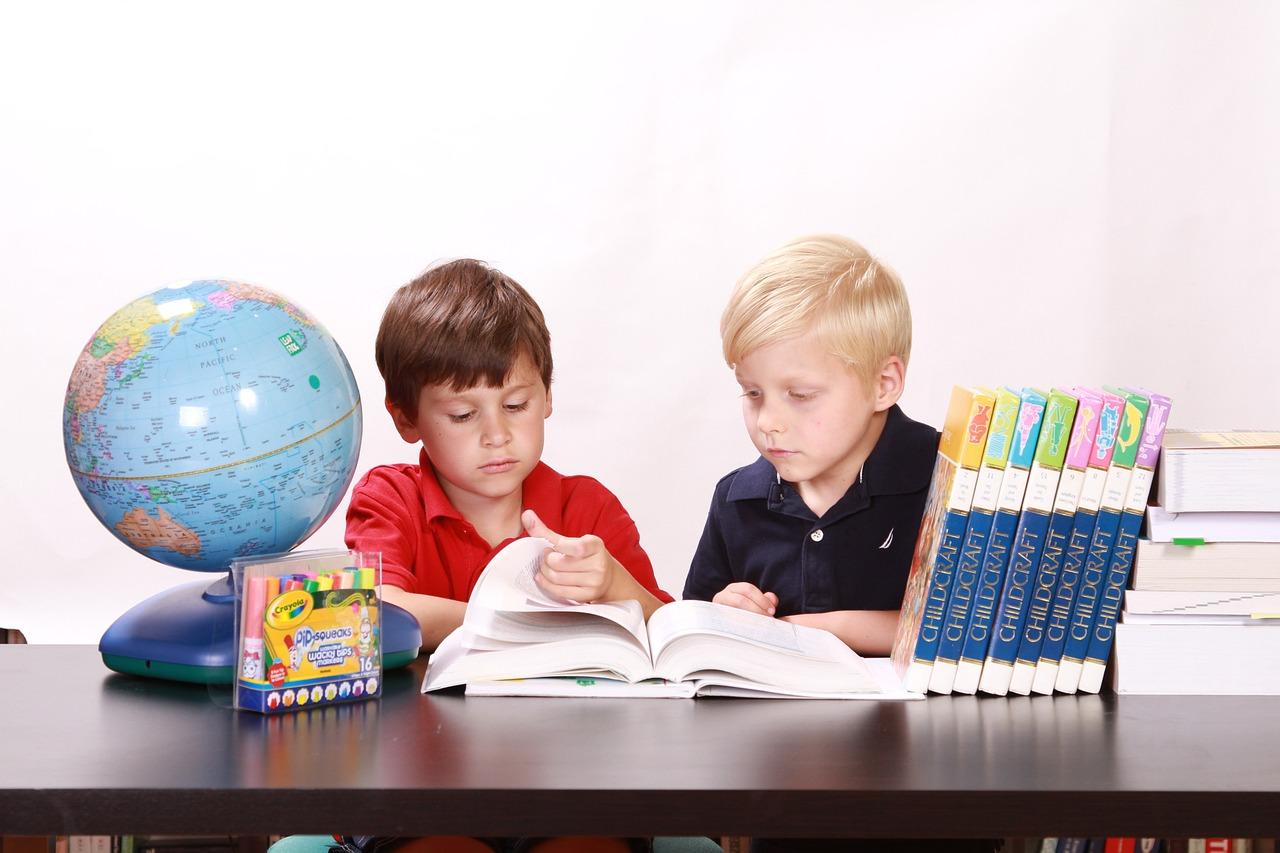 Two kids learning together at a table with books and a globe