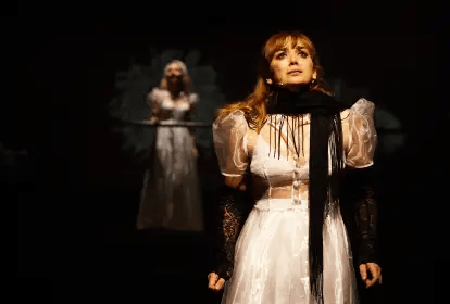 Cena teatral com mulher em primeiro plano sob iluminação de palco