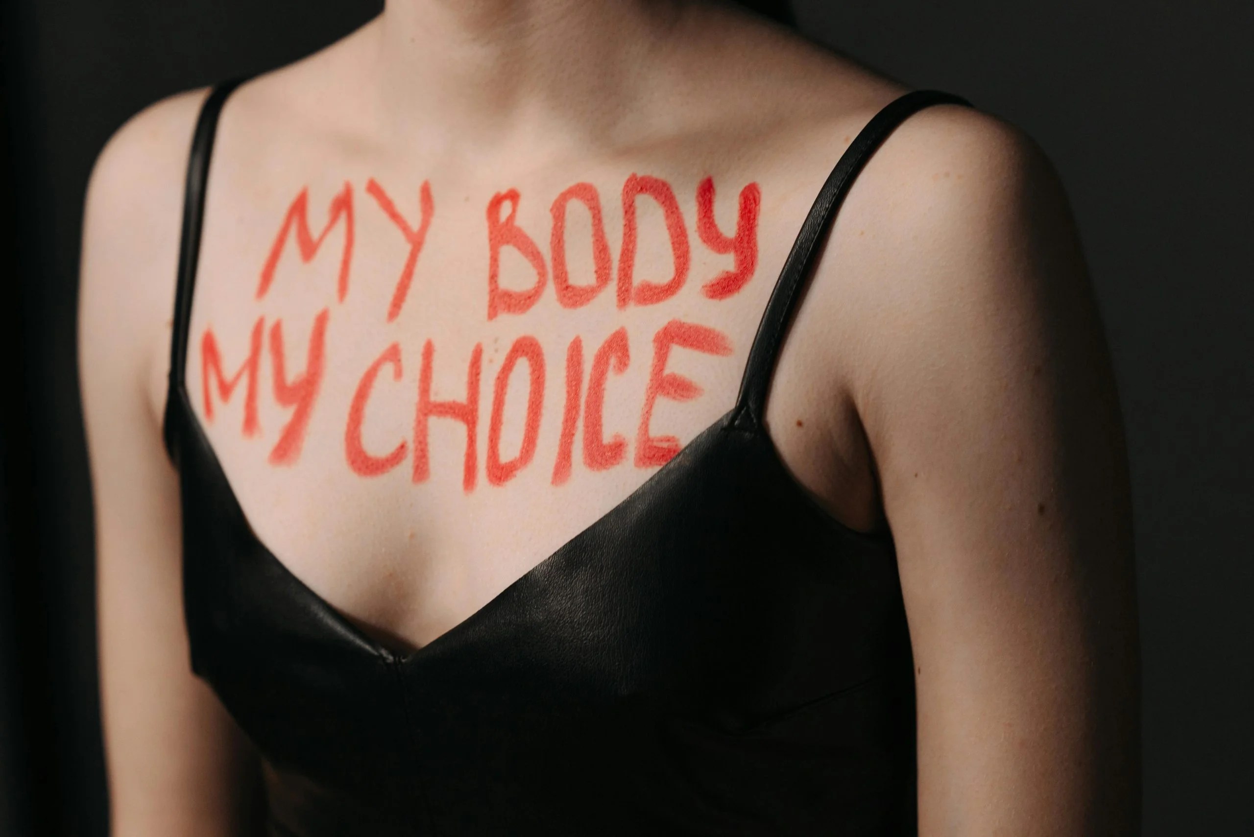 Close-up of empowering feminist slogan 'My Body My Choice' on woman's chest in black dress.