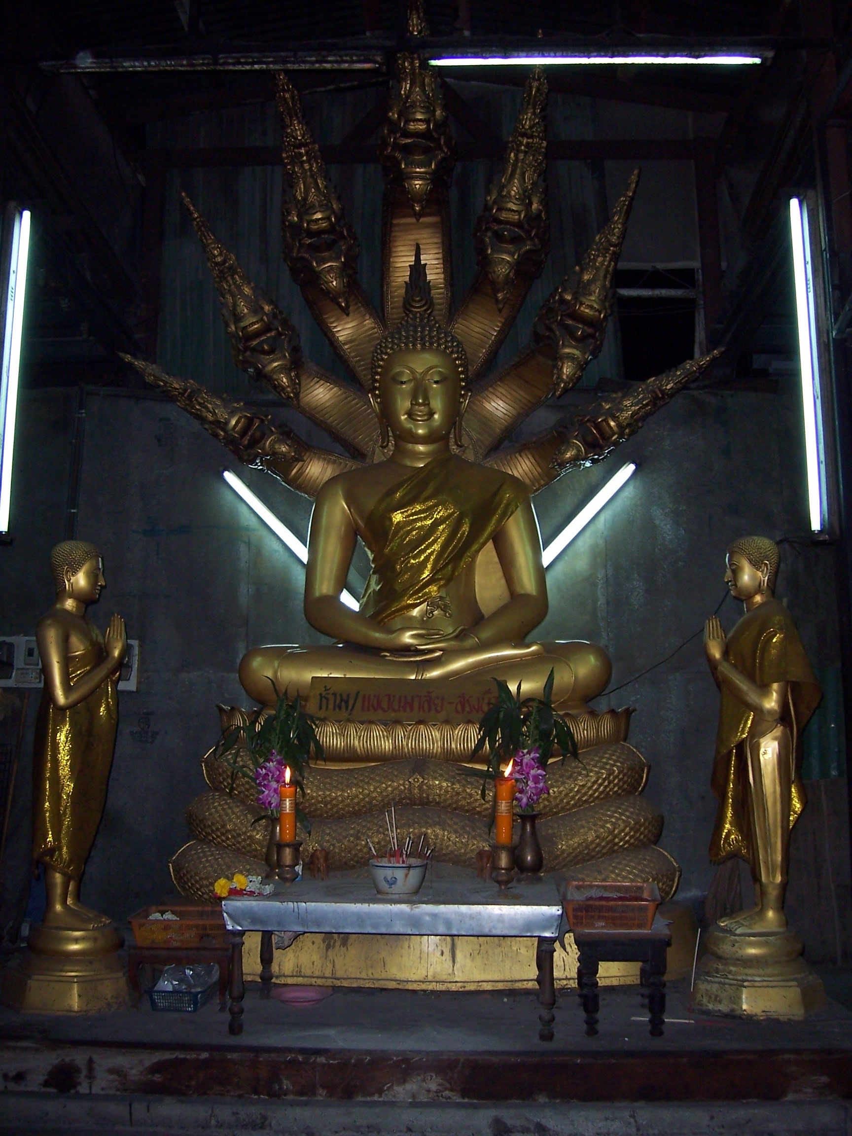 In Bangkok, an old bus shelter on the sidewalk of a busy street has been converted into an altar for Buddhist offerings. This elaborate and unlikely display is an outpost in the secular world, aiming to engage passersby on a busy street.