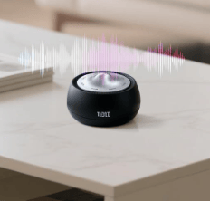 A black tabletop speaker with a sleek design on a light-colored marble surface, accompanied by an audio waveform graphic above it.