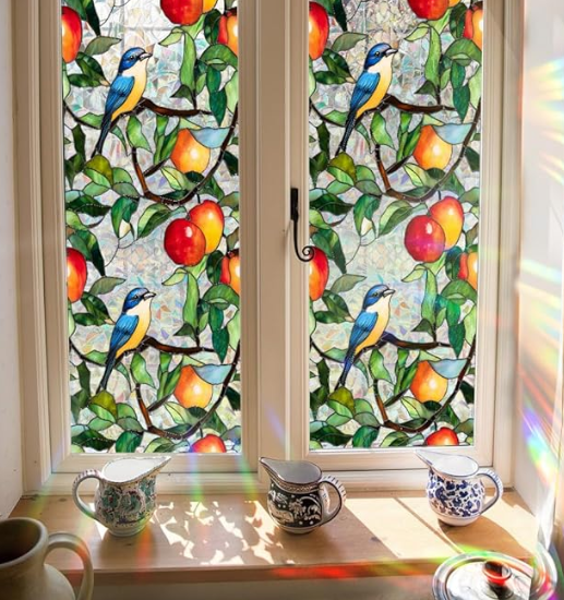 Stained glass window featuring blue birds and colorful fruits, with sunlight illuminating the glass, alongside decorative pottery on a windowsill.