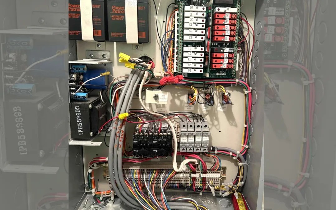 Technician performing elevator code compliance testing on control systems.