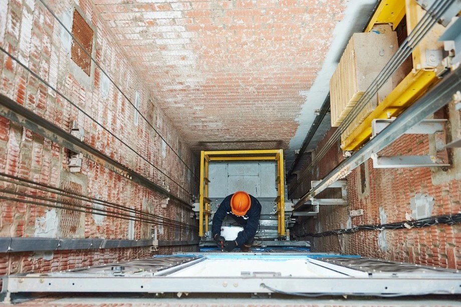Technician performing elevator maintenance inside a shaft, inspecting components and ensuring safe operation