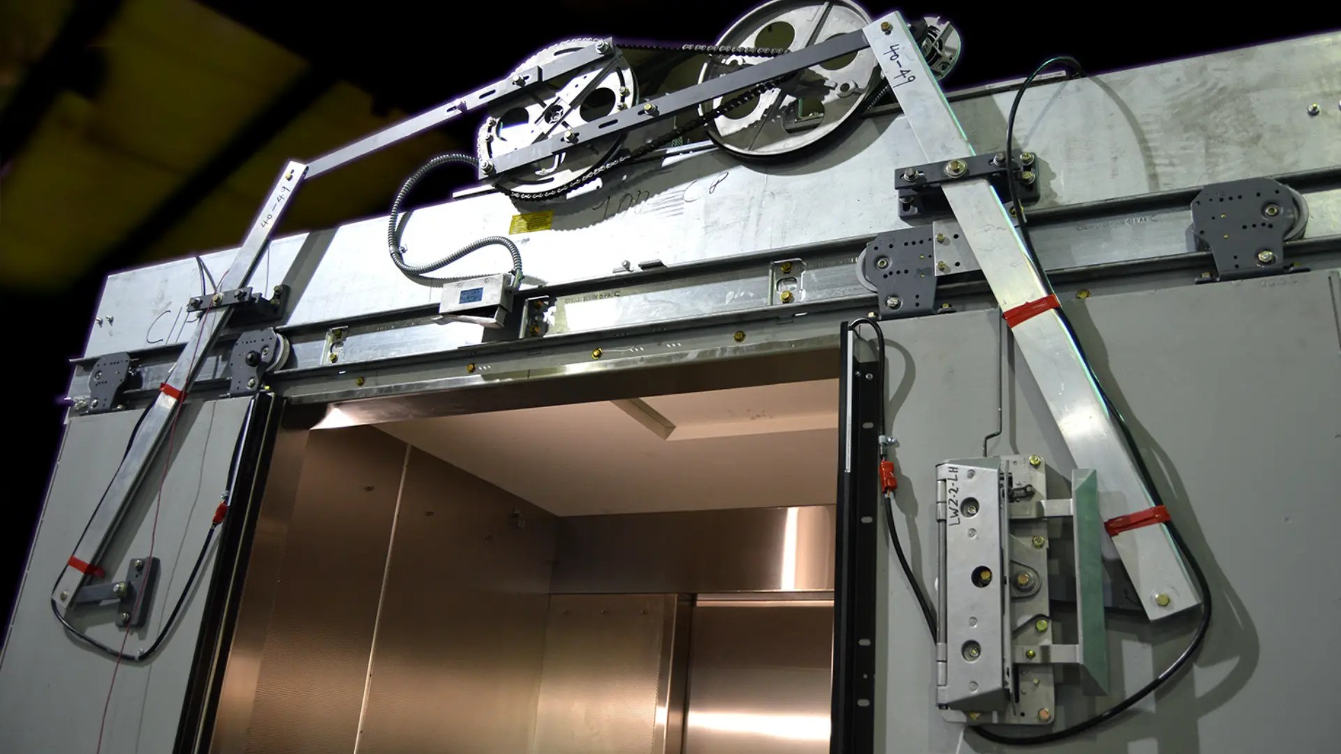 Elevator door mechanism with tracks, rollers, and motor components exposed, showing internal door system operation
