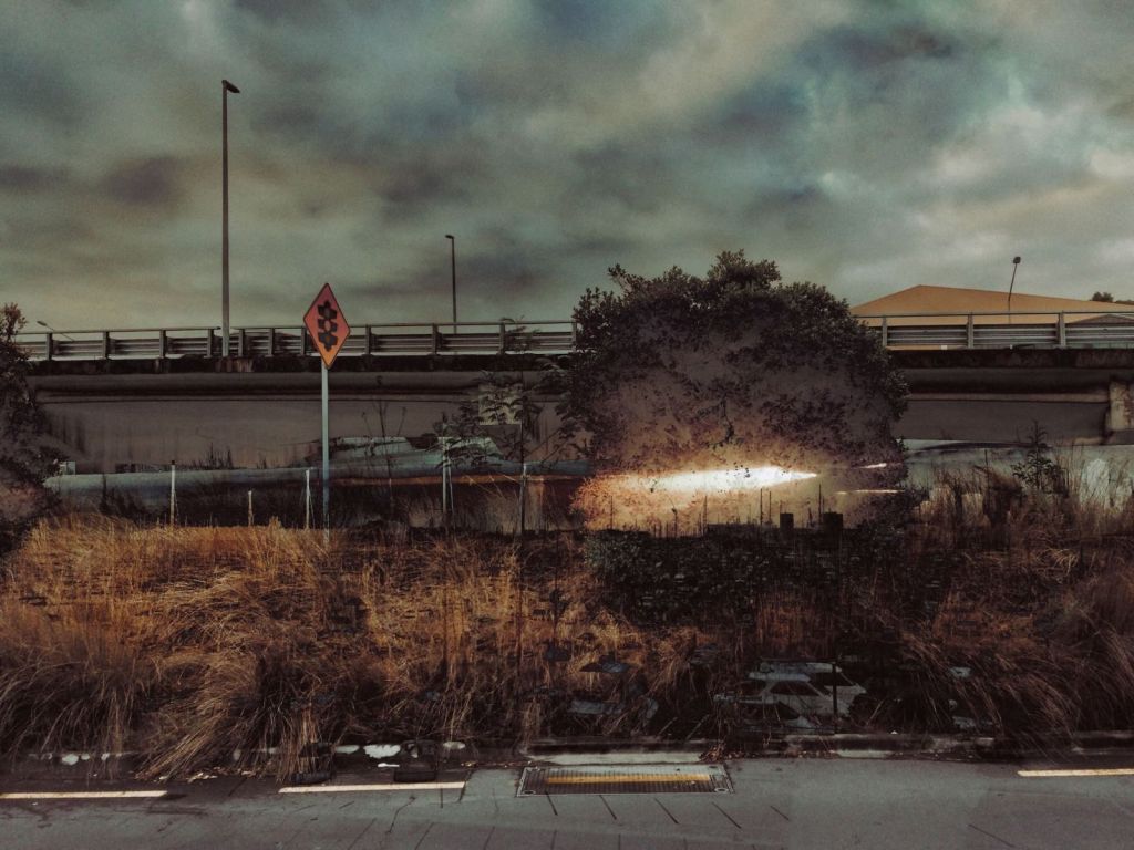 Altered multiple-exposure colour photograph of an urban roadside with dark clouds, dry vegetation and a bright burst of light spreading through a central tree.