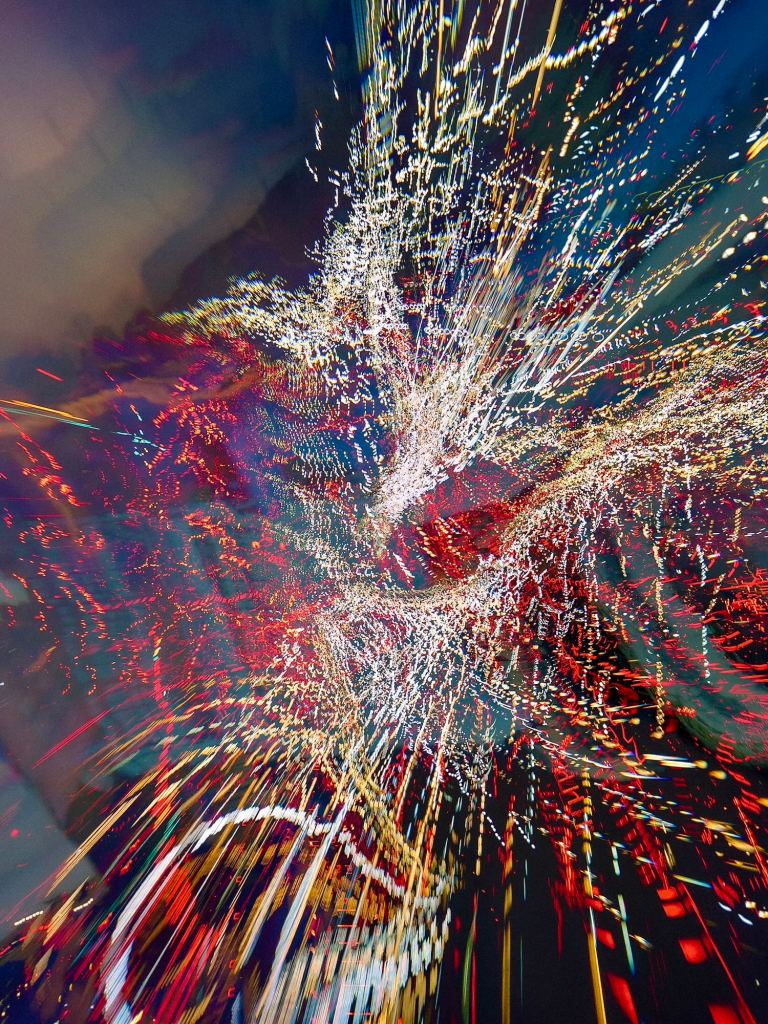 An abstract digital photograph with streams of red, gold, and teal radiating outward from a dense white-gold centre, with looping glitch artefacts and a faint suggestion of cloud in the upper left corner.