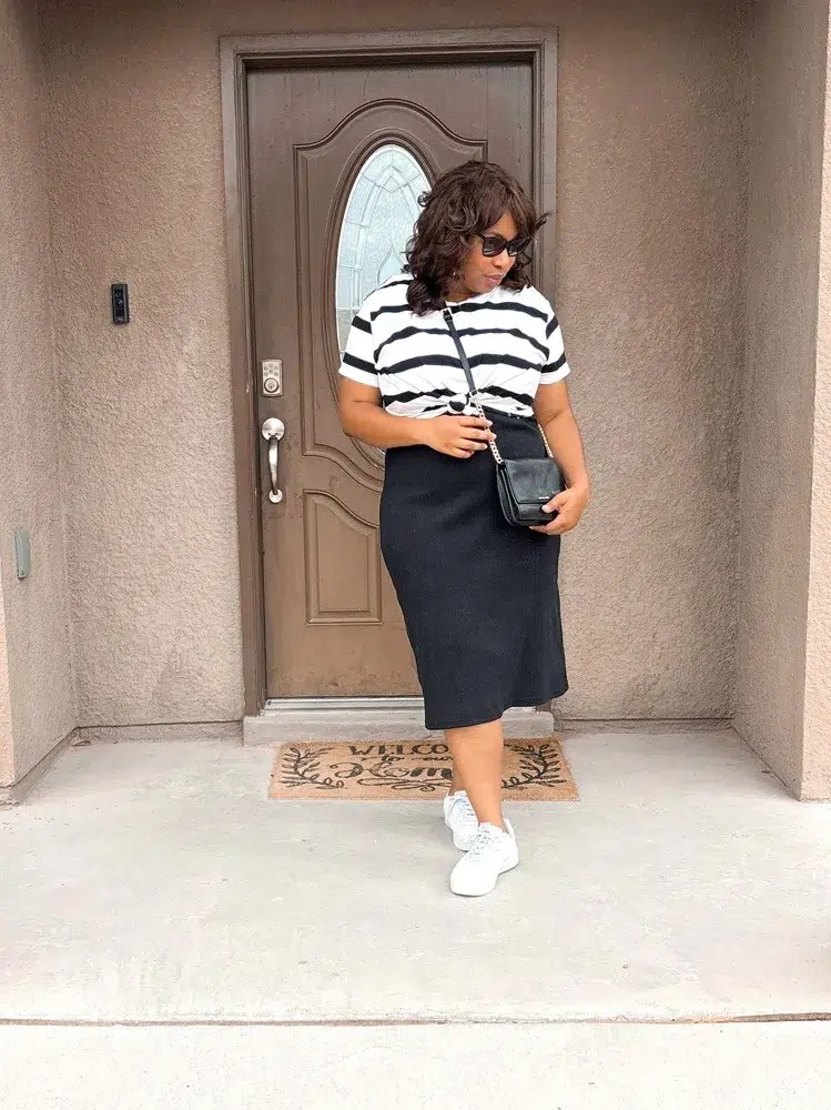 african american woman wearing a black and white striped t-shirt over a black tank dress with white sneakers