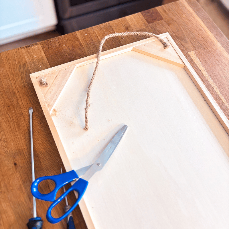 Picture of the back of the board on a table with an attached string cut on one side. A pair of scissors laying on the board.
