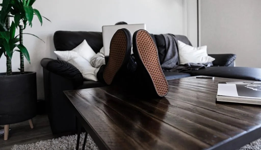 person sitting on couch with legs on coffee table holding a laptop
