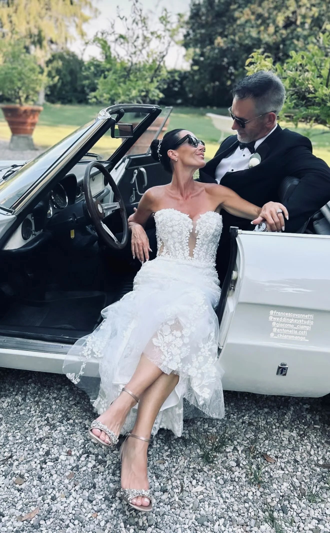 Bride and groom celebrating together beside a classic convertible car
