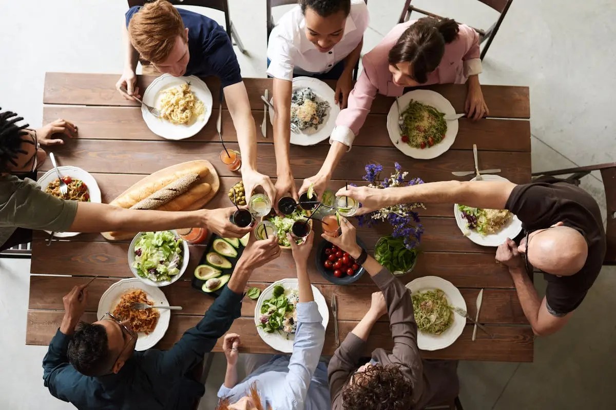 A group of people joyfully toasting with glasses over a beautifully arranged dinner table filled with various dishes and fresh salads.