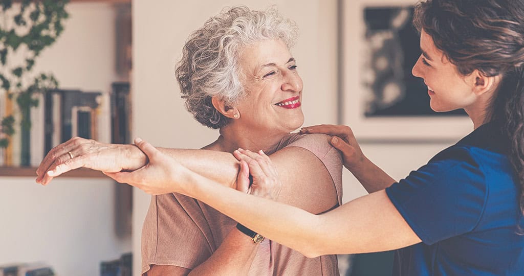 Caregiver helping senior woman stretch her arm across her body