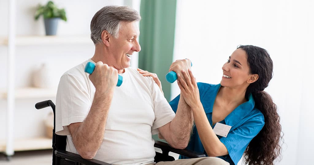 Female caregiver helping senior man in wheelchair lift weights