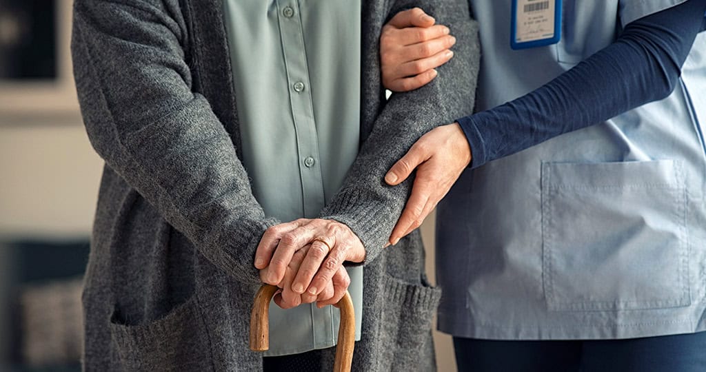 Caregiver helping woman holding cane walk