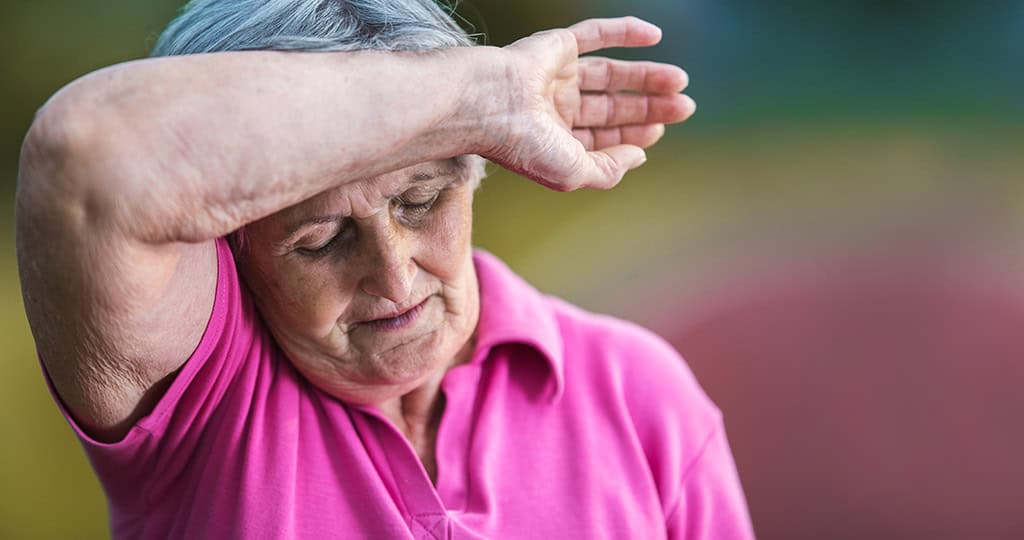 Elderly woman holding back of wrist against forehead due to heat