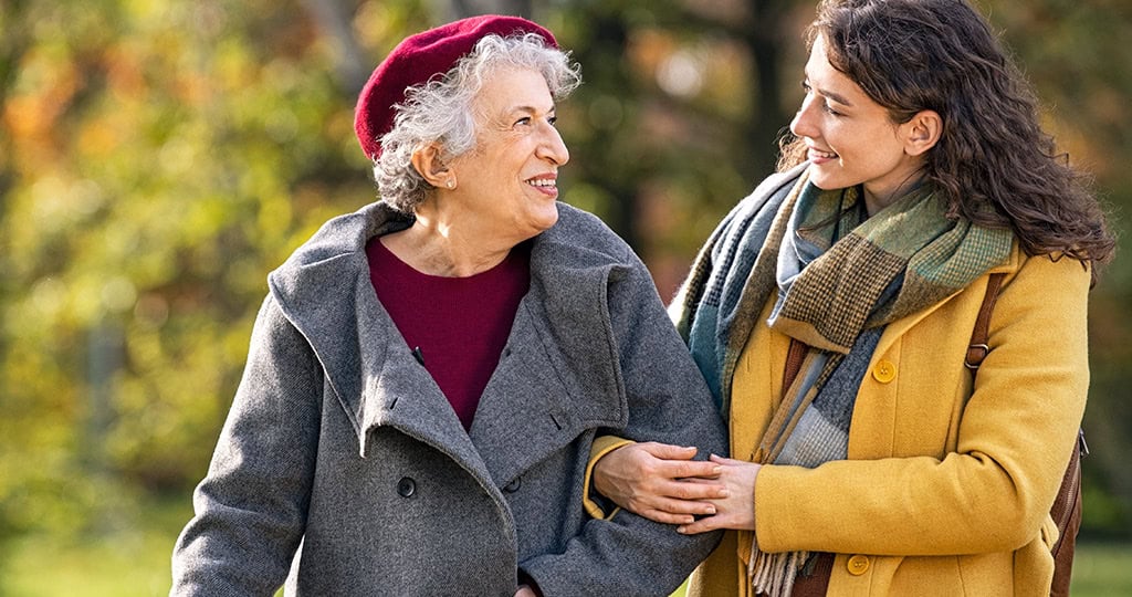 Smiling senior woman walking outside with caregiver