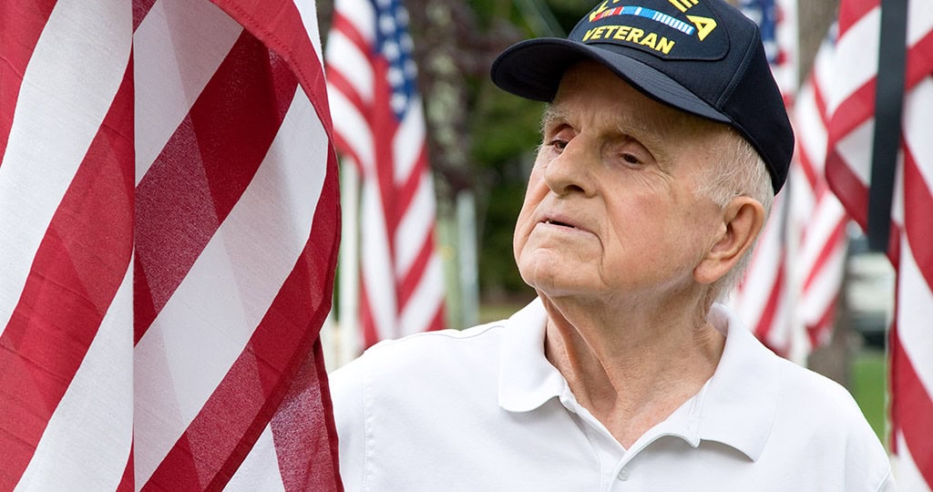 Senior veteran wearing Korea War hat looking at American flag
