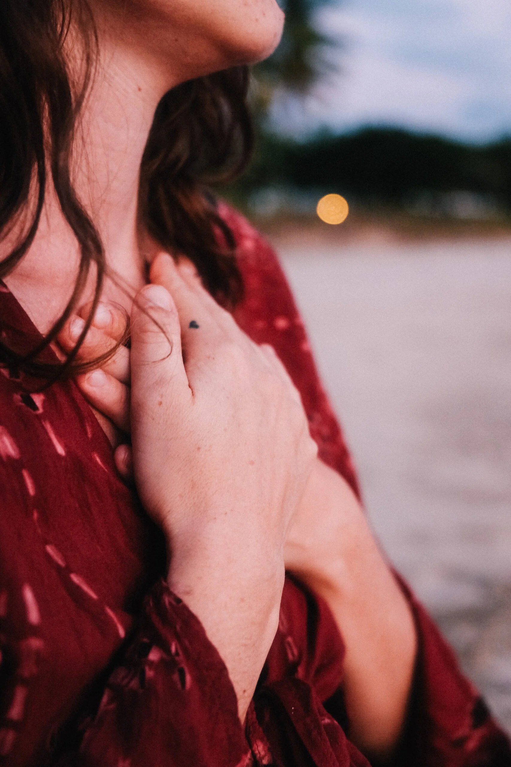 A woman in a red dress connects with herself through a heart-centered practice at a somatic healing retreat by the beach.