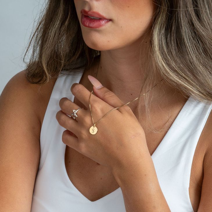Woman in a white tank top wearing an initial necklace.