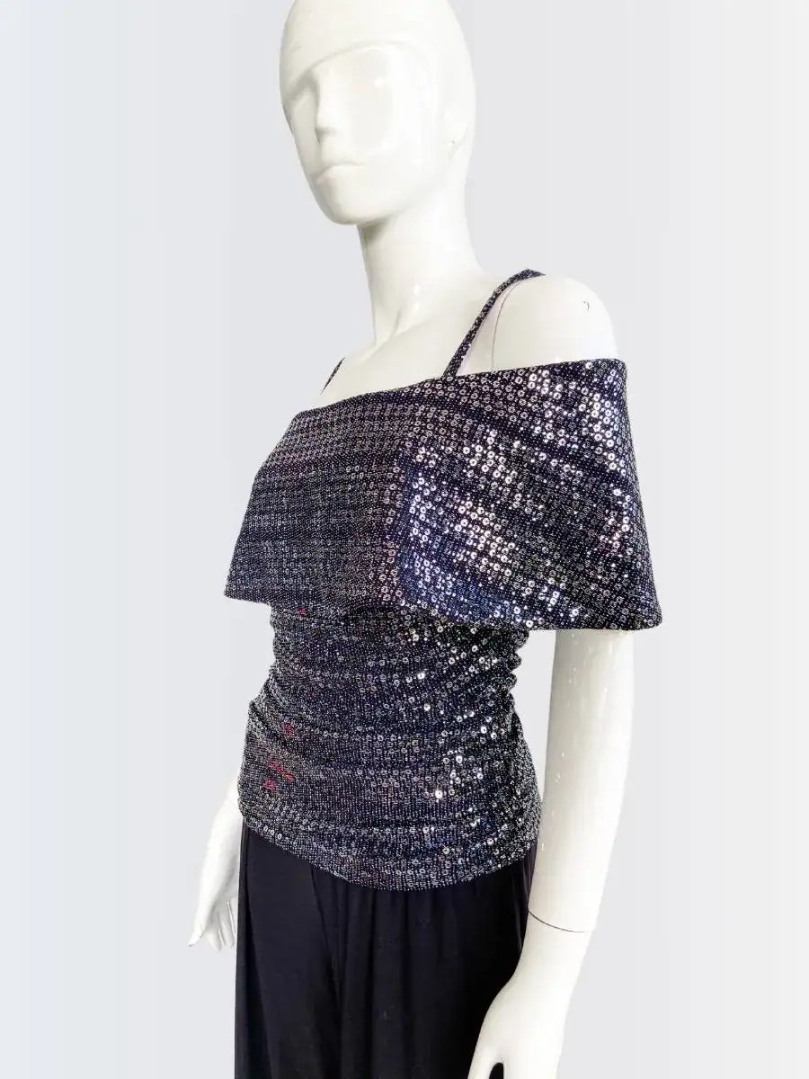 Maniquí vistiendo un jumpsuit de pantalón largo negro con top brillante de lentejuelas en tonos plata y azul, hombros descubiertos y tirantes finos. Diseño elegante y moderno, ideal para ocasiones nocturnas y eventos especiales.