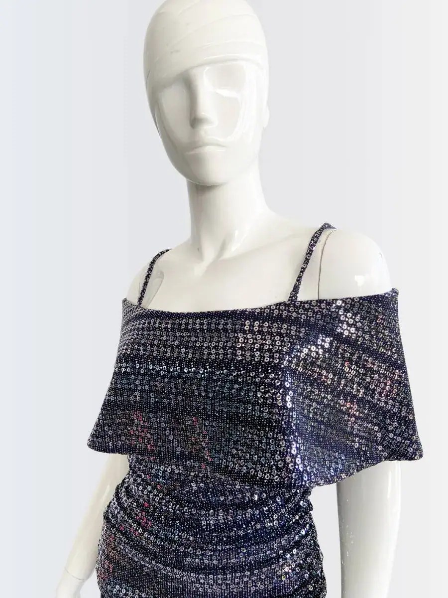 Maniquí vistiendo un jumpsuit de pantalón largo negro con top brillante de lentejuelas en tonos plata y azul, hombros descubiertos y tirantes finos. Diseño elegante y moderno, ideal para ocasiones nocturnas y eventos especiales.