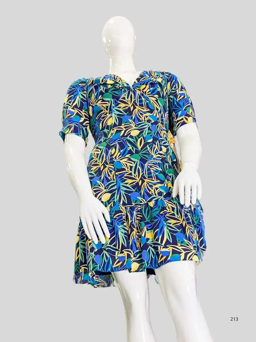 Maniquí vistiendo un vestido de mujer con estampado de hojas en tonos azules, verdes y amarillos, escote V y falda con vuelo, fotografía sobre fondo gris.