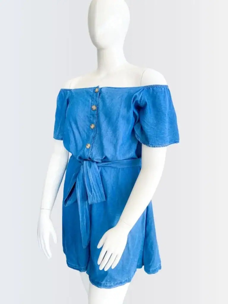 Romper azul tipo denim con hombros descubiertos y botones, lucido por el maniquí­ Francisca con fondo gris claro.