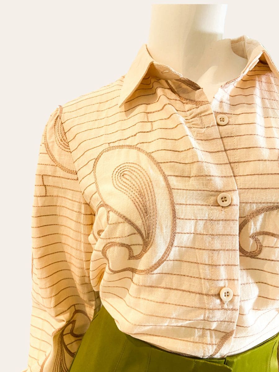 Maniquí vistiendo blusa camisera de mujer con ilustraciones orgánicas y líneas suaves sobre fondo claro, combinada con pantalón de color.