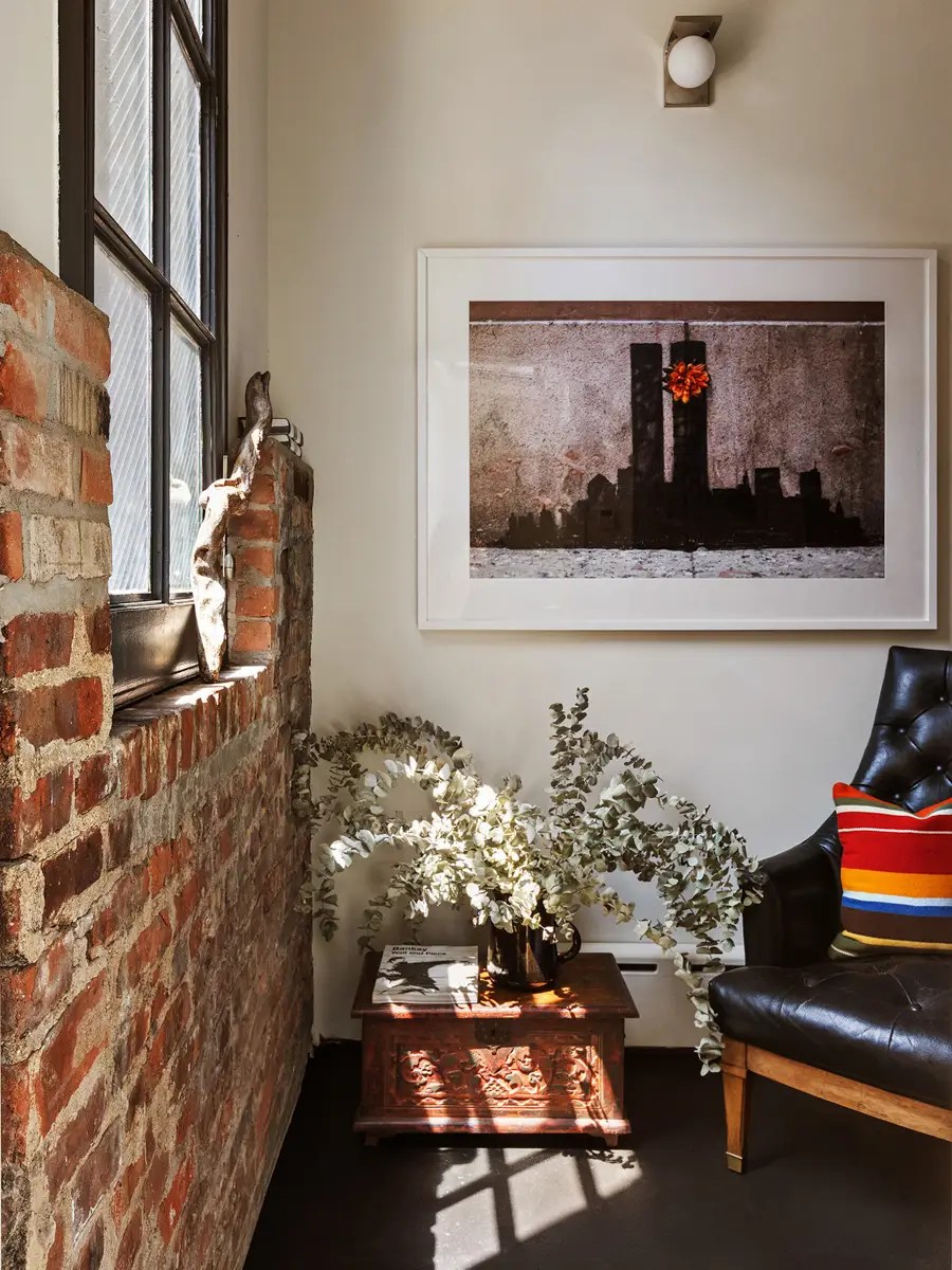 Brick reading nook with a black leather tufted chair, striped pillow, and a framed vintage Twin Towers photograph