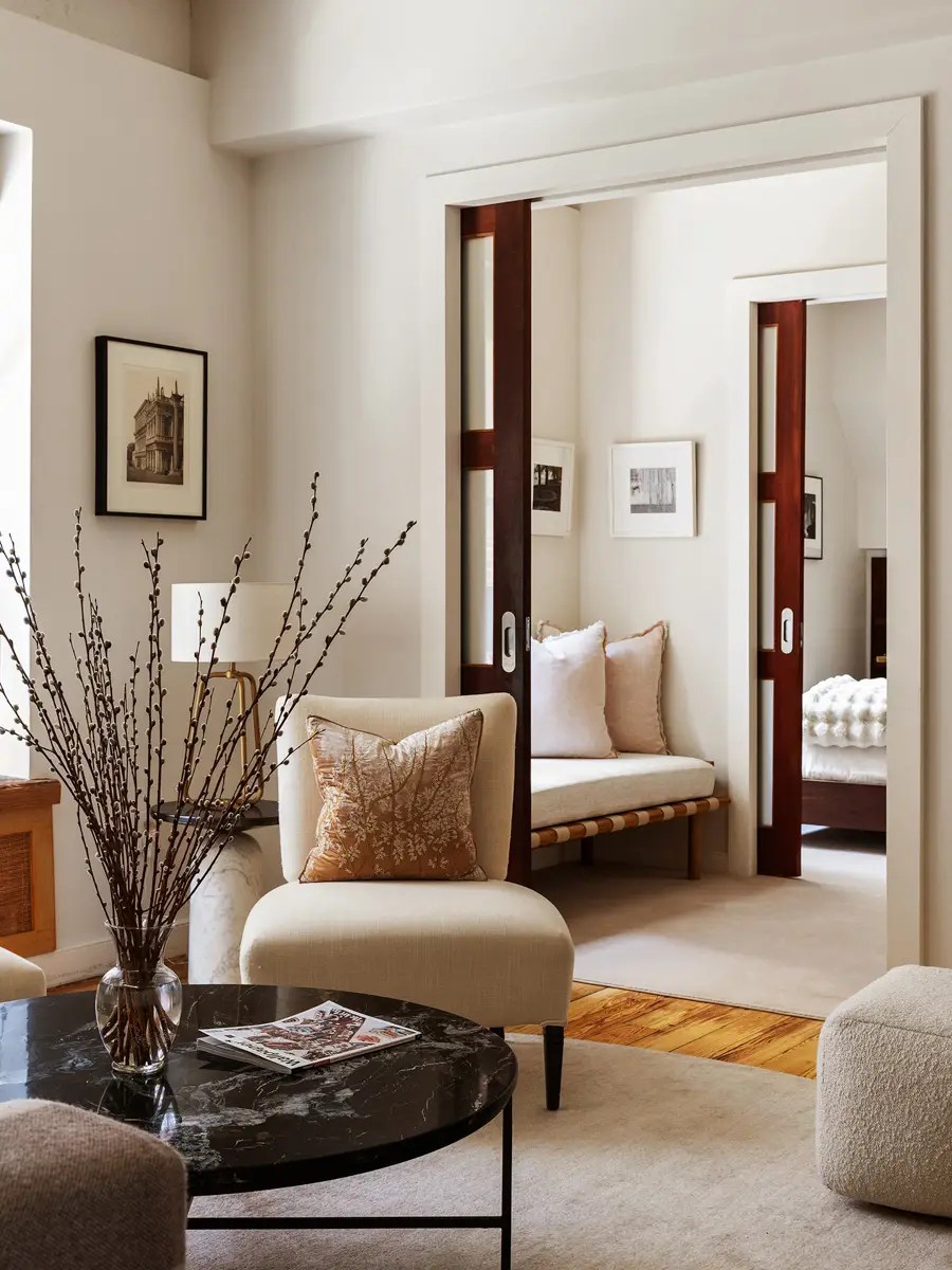 Living room with a cream slipper chair and marble table, opening through pocket doors to a daybed nook
