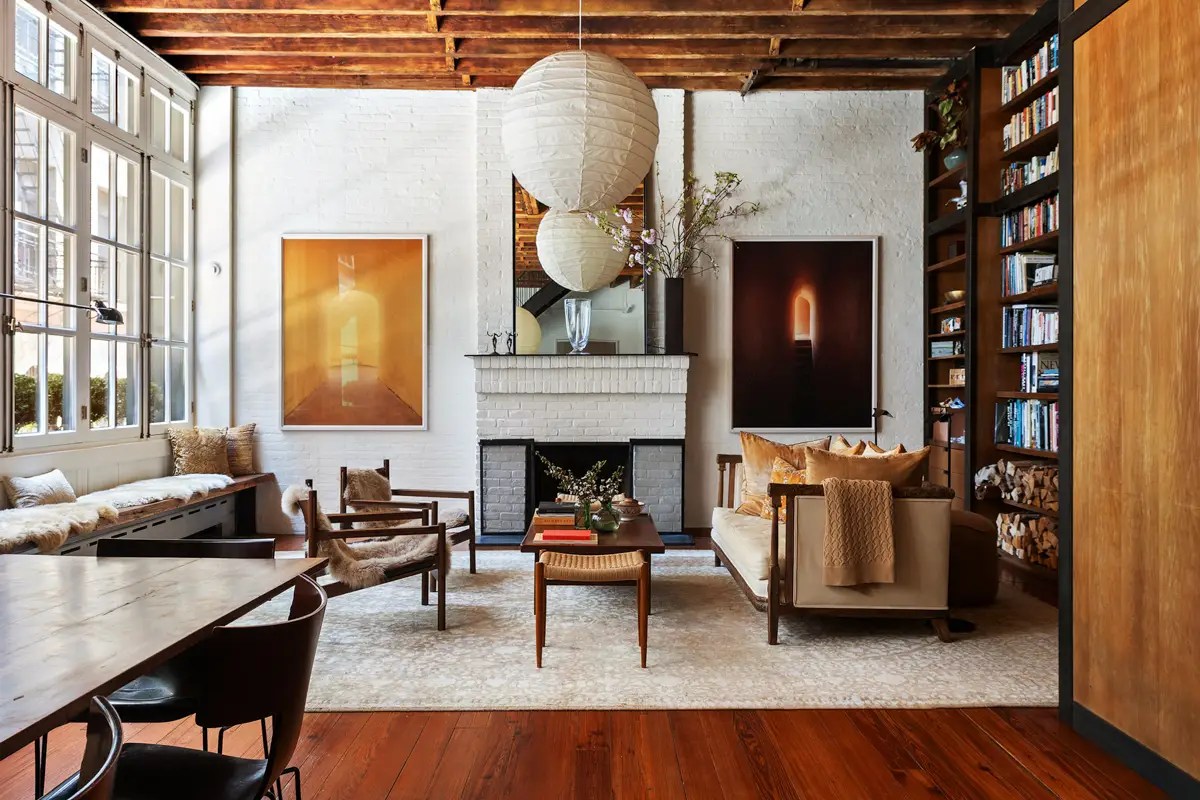 Loft living room with exposed wood ceiling beams, paper globe pendants, a whitewashed brick fireplace, and built-in bookshelves