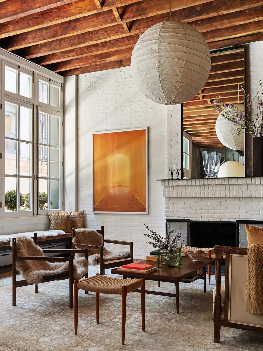 Sitting area with sheepskin-draped wood-frame chairs, a whitewashed brick fireplace, and warm amber artwork