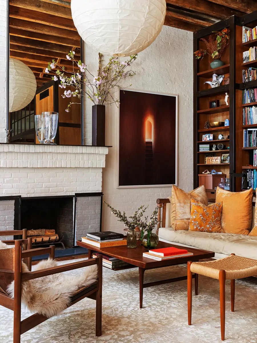 Reading corner with a woven bench, velvet pillows, built-in bookshelves, and a fireplace mantel with paper lanterns