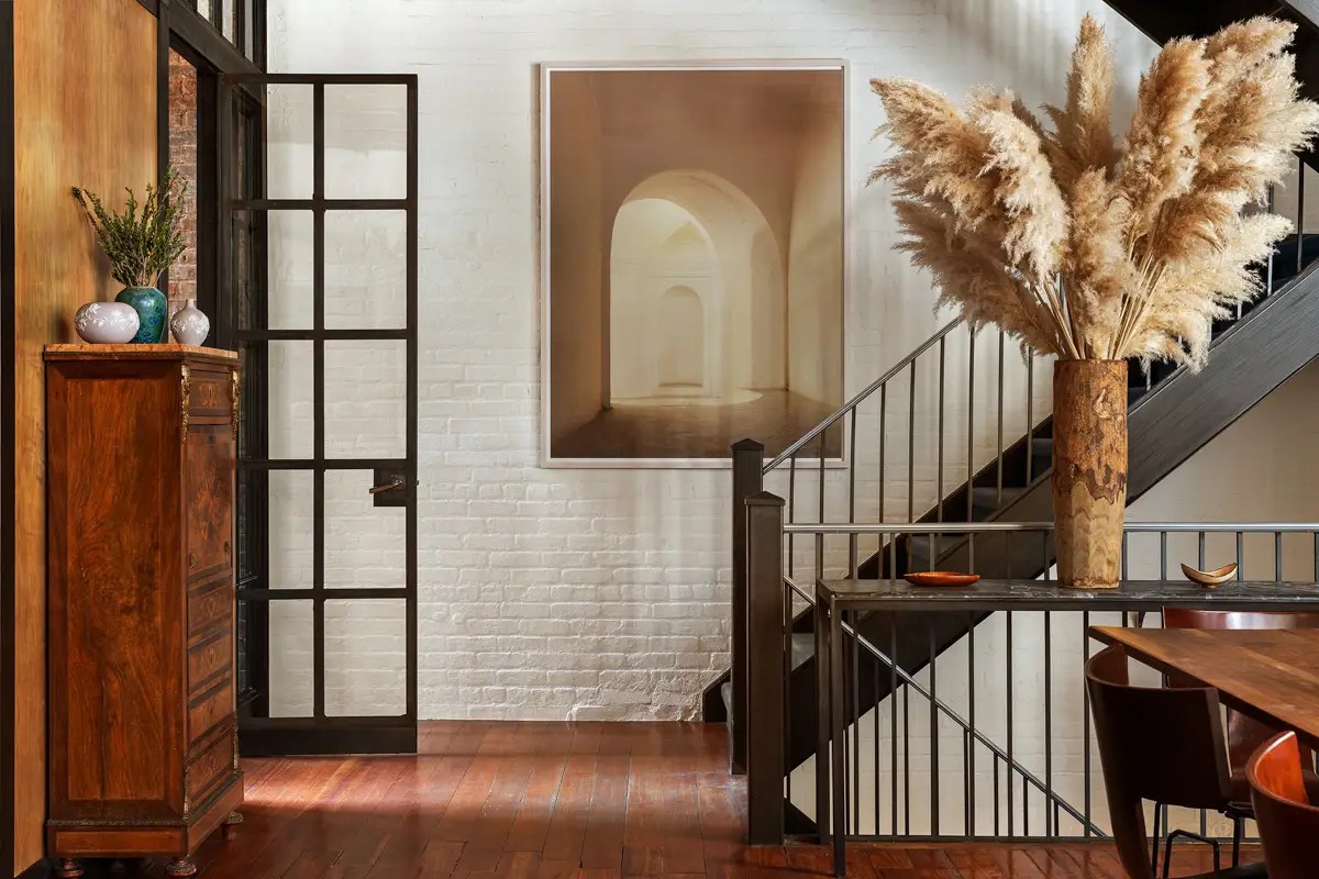 Entry hall with an antique wood chest, black steel-framed door, pampas grass arrangement, and a glowing archway photograph