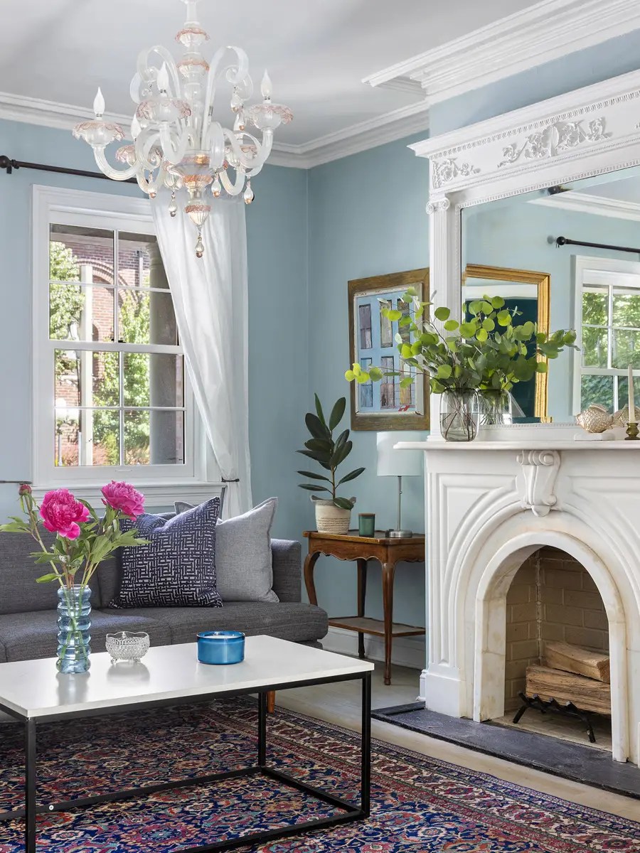 Powder-blue parlor with a crystal chandelier, carved marble mantel, and a gray sofa on a Persian rug