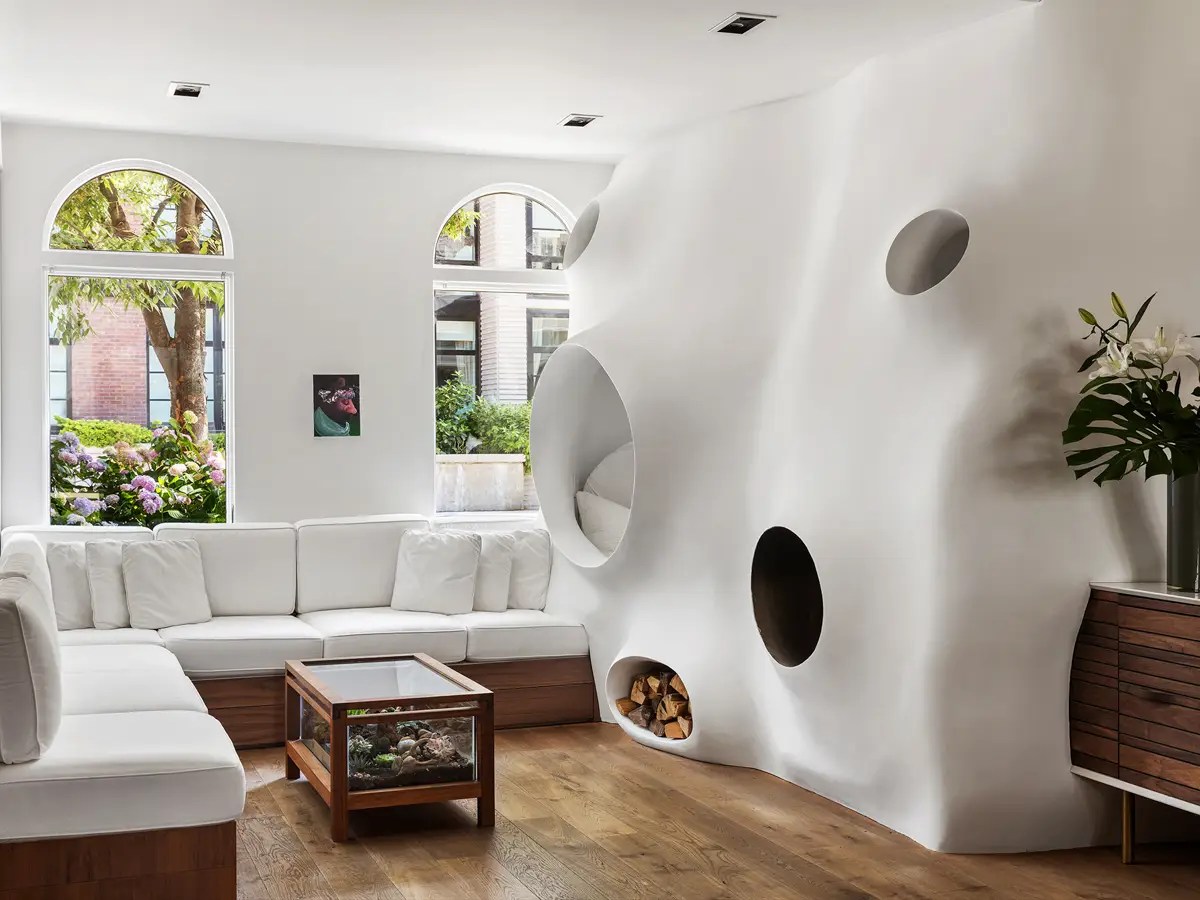 Sculptural white plaster wall with organic oval niches and a firewood cubby beside a white sectional sofa