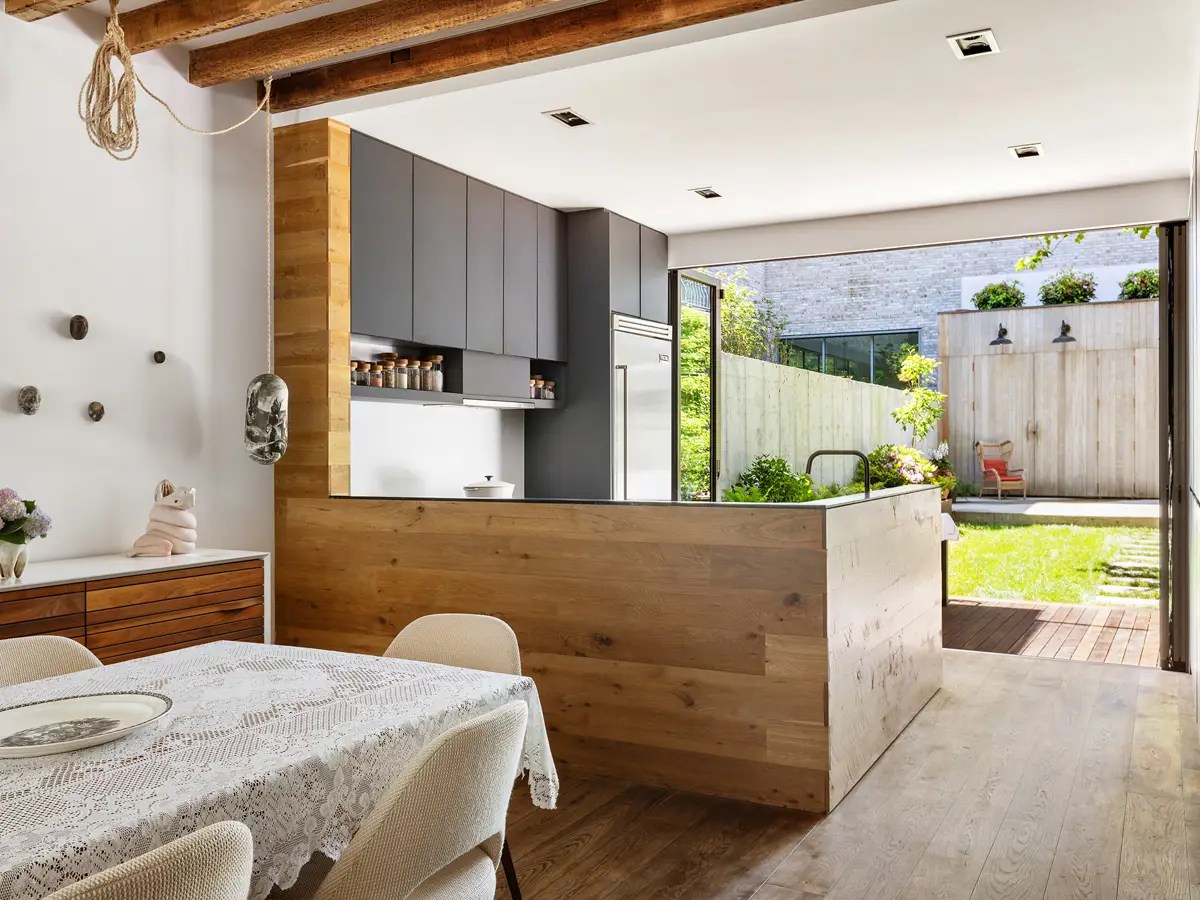 Reclaimed-wood kitchen island opening through folding glass doors to a fenced backyard with a wood privacy wall