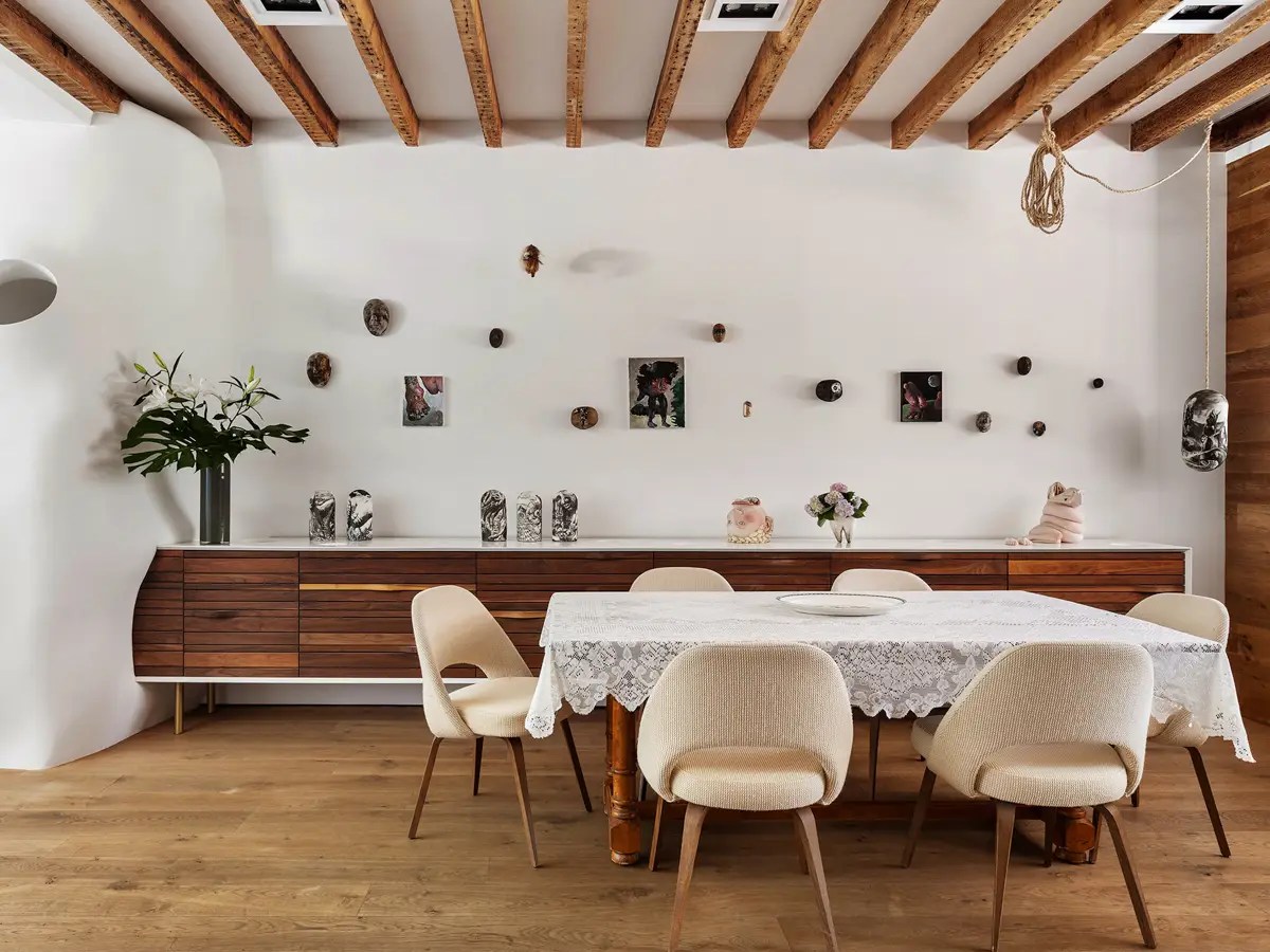 Dining room with a lace-covered farm table, cream Saarinen-style chairs, and a wood credenza displaying folk art