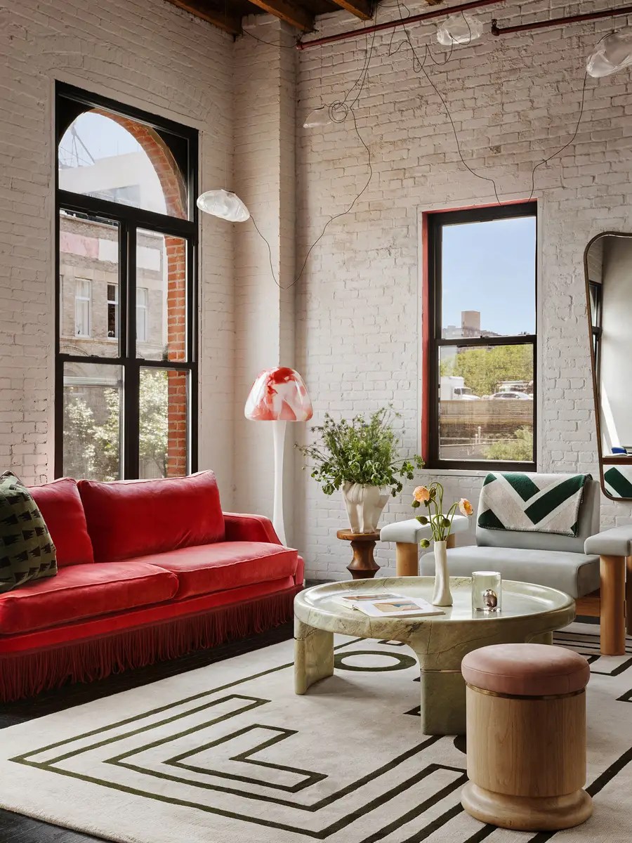 Brick loft living room with a red velvet fringed sofa, green geometric rug, and a green marble coffee table