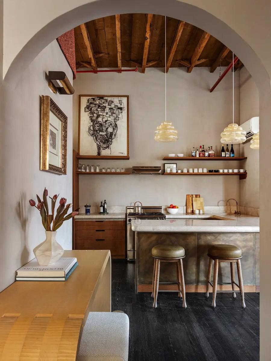 Archway framing a wood-beamed kitchen with amber pendant lights, marble counters, and leather counter stools