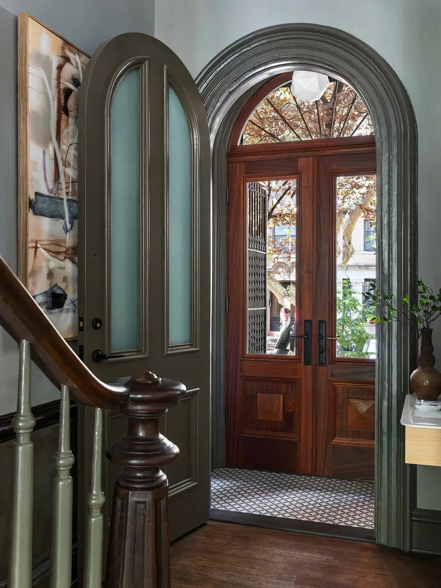 Entry vestibule with an arched mahogany door, patterned tile floor, and a curved wood stair rail
