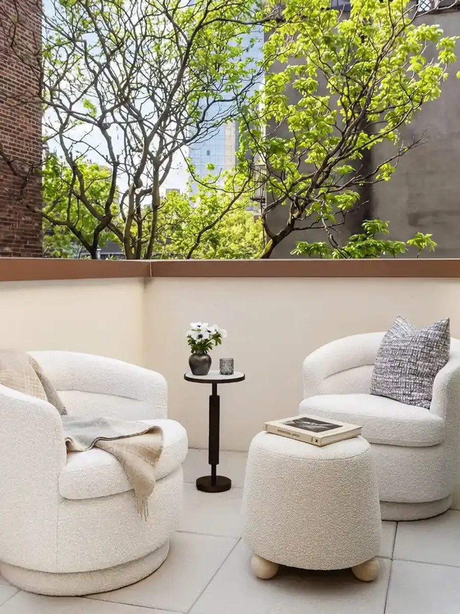 Rooftop terrace seating area with white bouclé swivel chairs and ottoman, framed by city views
