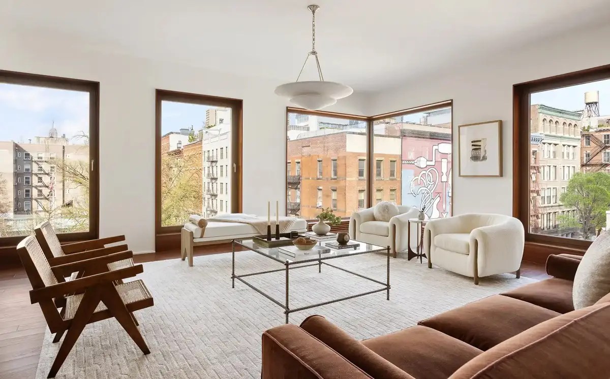 Corner living room with floor-to-ceiling windows, cane lounge chairs, and a brown velvet sofa overlooking the city