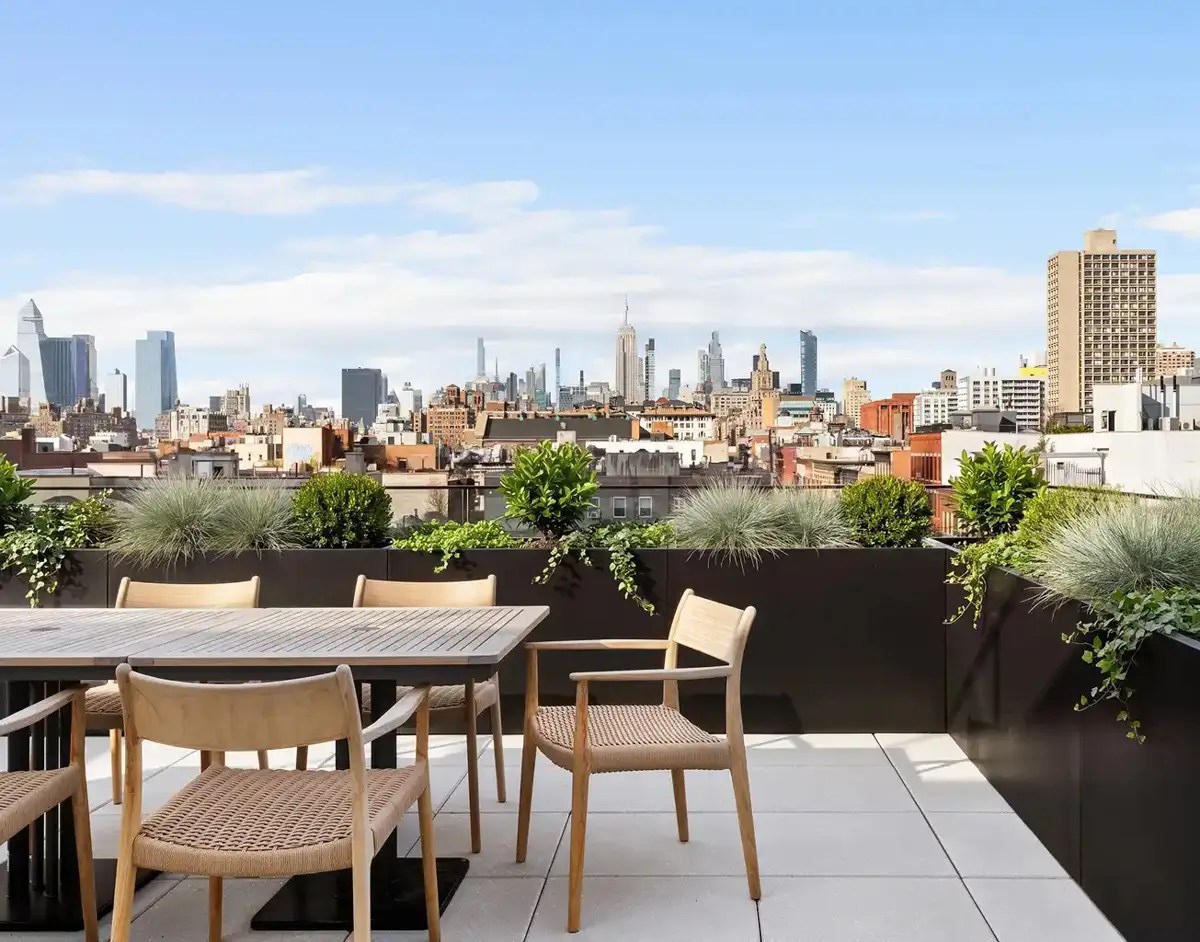 Rooftop dining terrace with a wood table and woven chairs overlooking the Manhattan skyline