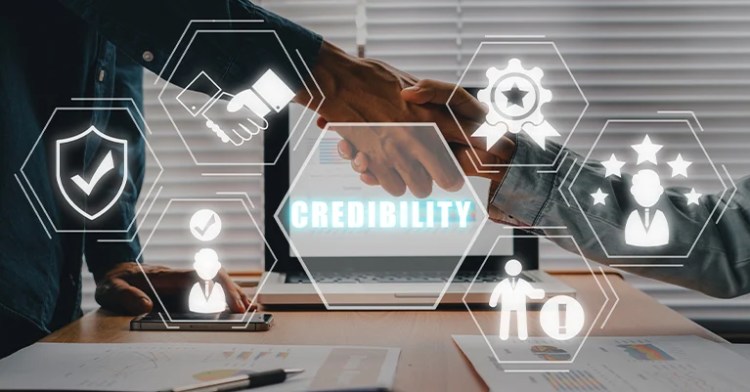 BrandCred_1 • Andrew Roche Two people shaking hands over a desk with the word "Credibility" on a screen and trust-related icons overlayed.