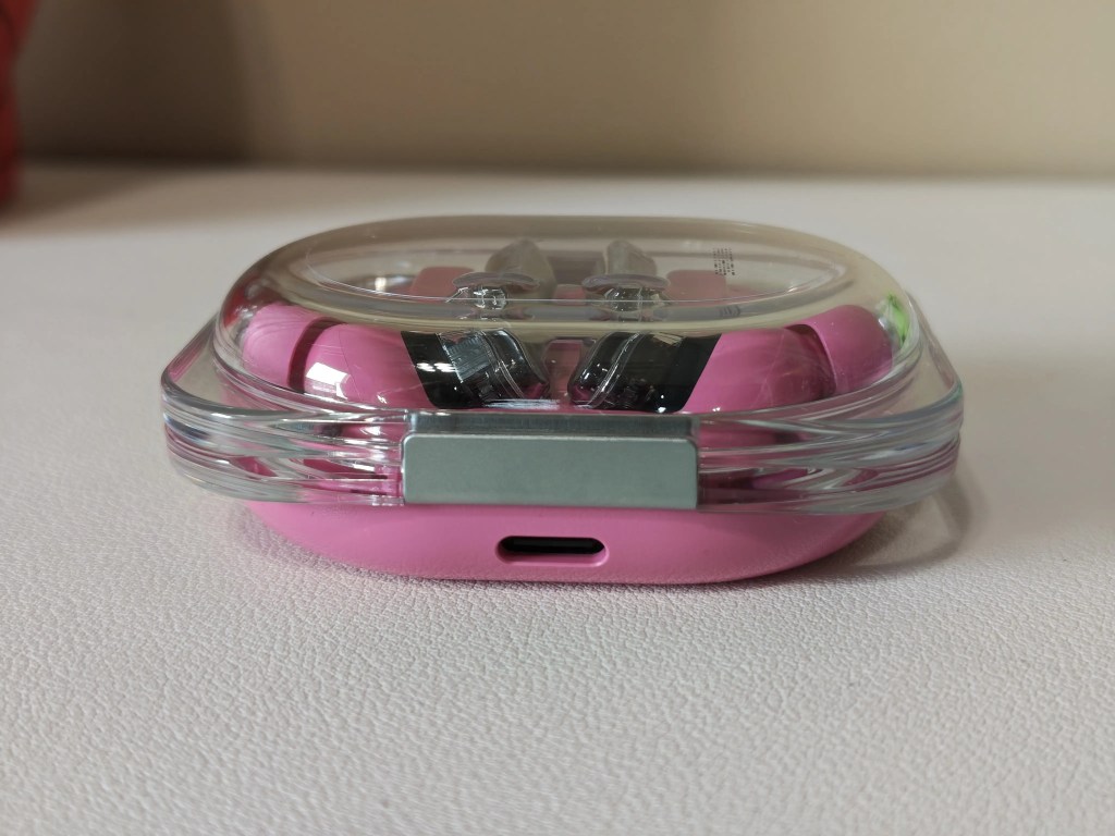 A pink earbud case with a transparent lid, showcasing the earbuds inside.