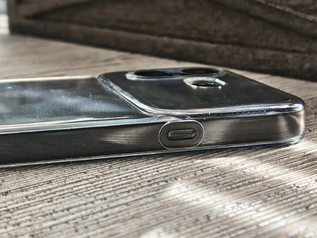 Close-up view of a smartphone with a clear case, showing the camera module and charging port on a textured surface.