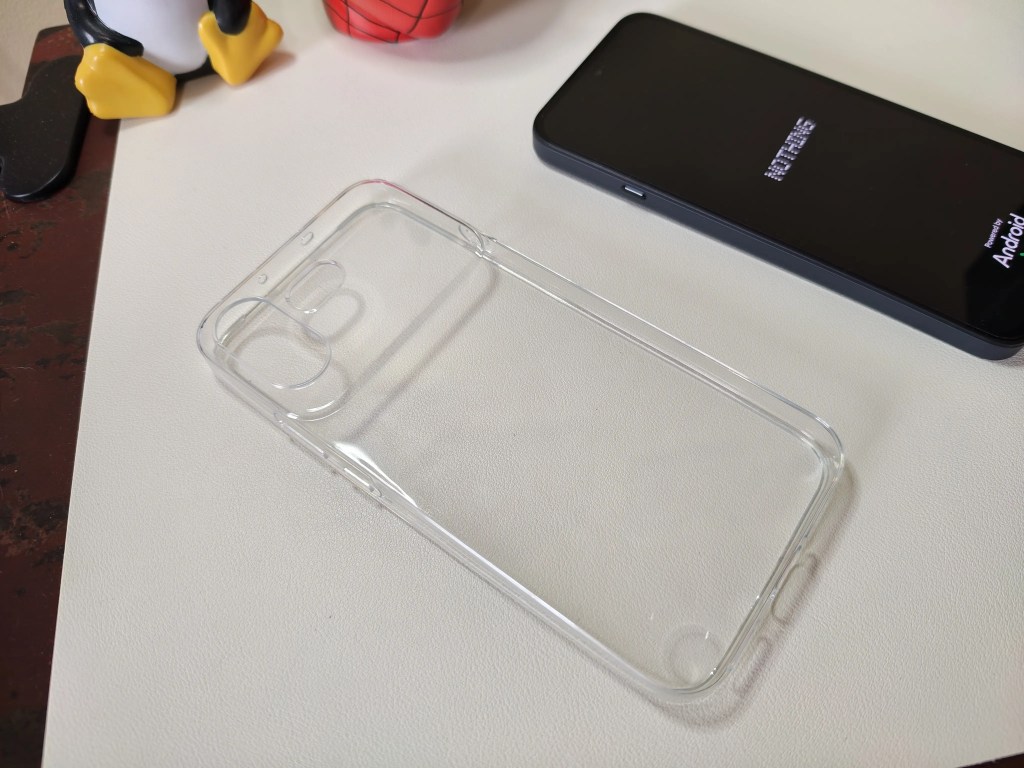 A transparent phone case placed on a light-colored surface next to a smartphone displaying the Android logo.