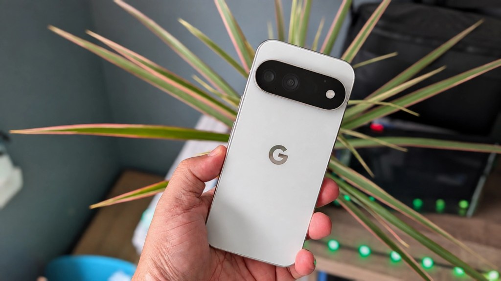 A close-up of a person holding a white smartphone featuring dual cameras and a 'G' logo, with a green plant in the background.